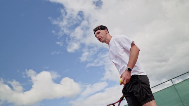 Caucasian young adult man practicing tennis serve with racket on outdoor court, shot from low angle. Clip fits sports marketing, tennis academy advertising, and athletic coaching campaigns