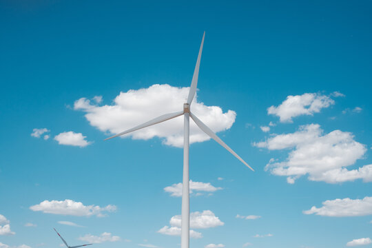 View of Wind farm Alibunar with a large white wind turbine standing against a bright blue sky with scattered white clouds in Alibunar, Vojvodina, Serbia.