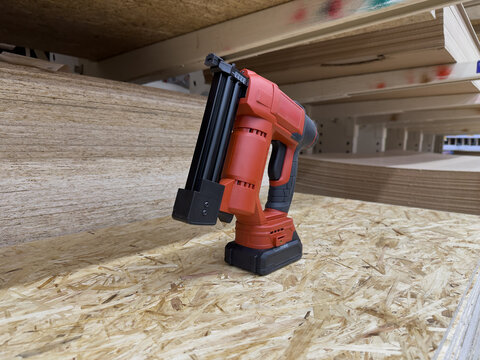 Battery-Powered Stapler on a Wooden Surface Among Shelves of Wood in a Workshop Setting, Highlighting Innovation in Construction Tools