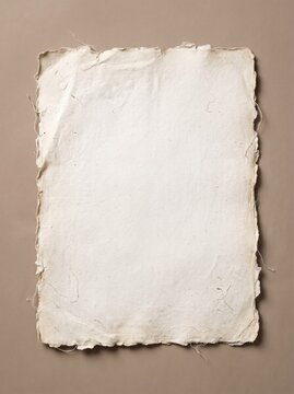 A blank sheet of handmade textured paper with rough, torn edges lies on a neutral beige background.