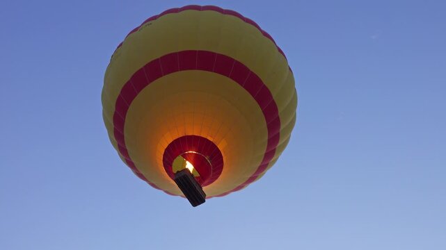View of a colorful hot air balloon with yellow and red stripes floating in the clear blue sky above Luxor Governorate, Egypt.