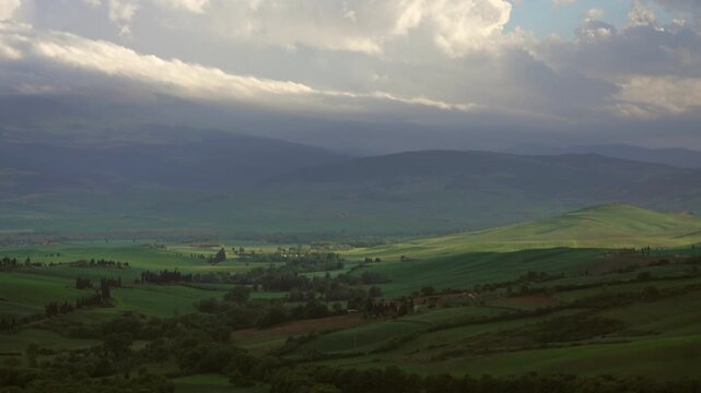 View of the rolling green hills and dramatic cloudy sky of the Tuscan landscape in Tuscany, Italy.