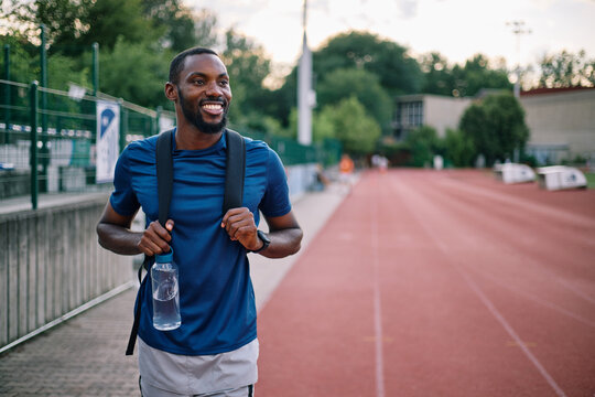 Smiling athlete carrying backpack and water bottle on track