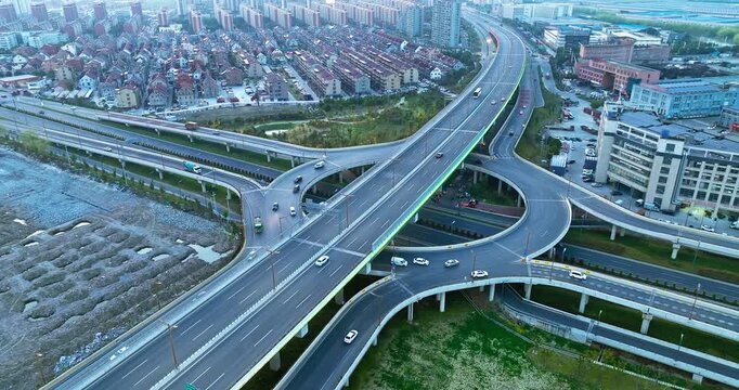 High-angle aerial view of a multi-level highway interchange with curved overpasses, multi-lane asphalt roads, and moving cars under soft daylight.
