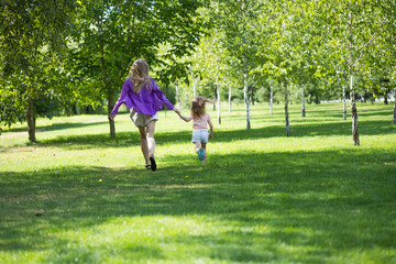 Fototapeta premium Distant shot of mother and young daughter running hand in hand in park
