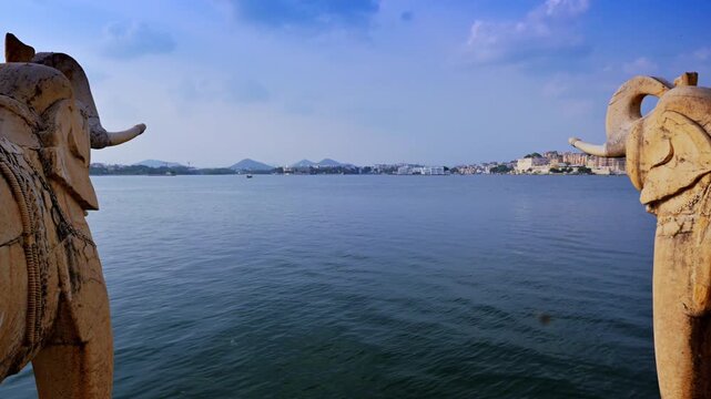 Carved elephant statues at Jag Mandir frame a view across Lake Pichola toward Udaipur's distant City Palace waterfront.