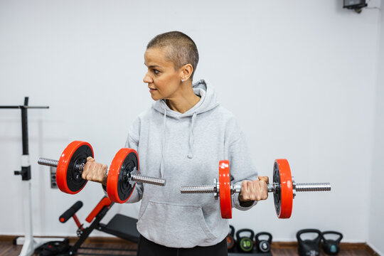 Determined sportswoman lifting dumbbells, exercising biceps in home gym