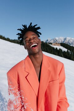 Smiling male model in coral blazer on snowy mountain for winter fashion portrait and lifestyle banner design