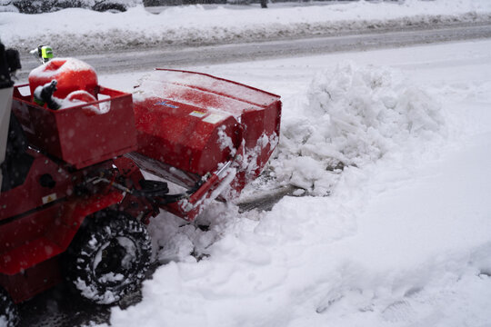 a red snow blower clearing deep snow from a street with piled snow and slushy pavement. Horizontal photo.