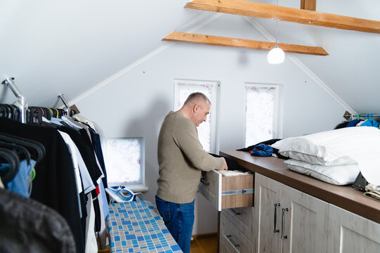 Man organizing a drawer in an attic room with clothes and bedding