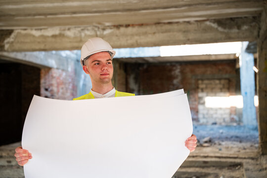 Construction professional holding large architectural plans inside an unfinished renovation building. Construction planning blueprint review and architectural design verification
