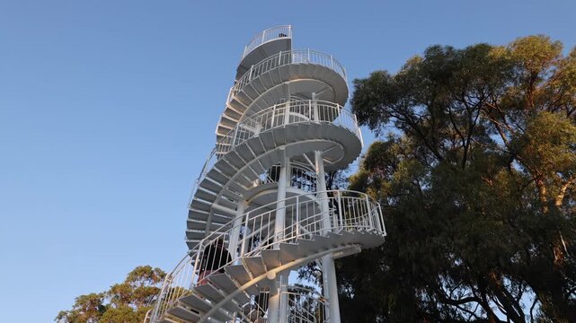 View of white spiral staircase in a park with stone paving and surrounding trees during golden hour in Perth, Western Australia, Australia.