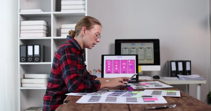 Woman ux designer working on mobile application user interface layout, creating wireframes and app prototypes on a computer at a creative office desk