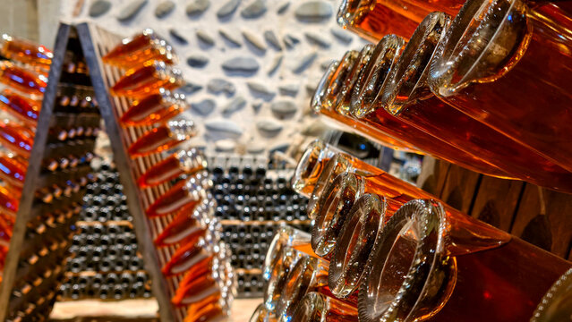 Rose sparkling wine bottles riddling on traditional A frames in a dark, historic stone cellar, symbolizing artisan craftsmanship, aging, and quality wine production