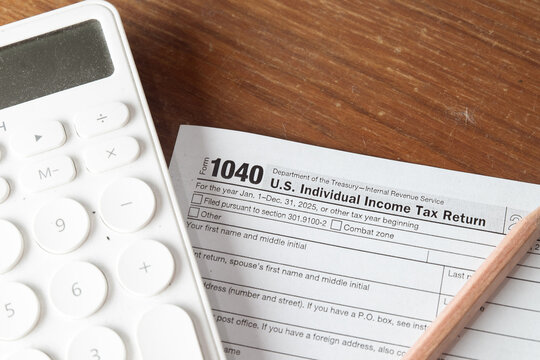 Close up of a US IRS 1040 Individual Income Tax Return form for 2025 with a white calculator and pencil on a wooden desk. Concept of tax season preparation, financial accounting, and income refund.
