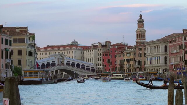 View of the iconic Rialto Bridge over the Grand Canal with traditional gondolas and water taxis navigating the waterway in Venice, Veneto, Italy.