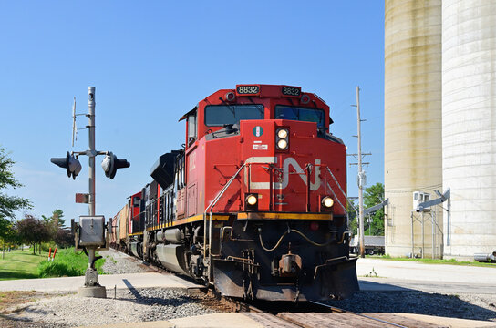 A pair of locomotives lead a Canadian National Railway merchandise freight train northbound through a grade crossing and past grain elevators in a small north central Illinois community.
