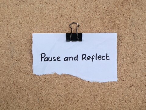 Pause and reflect inspirational message written on torn white paper held by a black binder clip on a cork board background. Flat lay concept for mindfulness, mental health, and self improvement