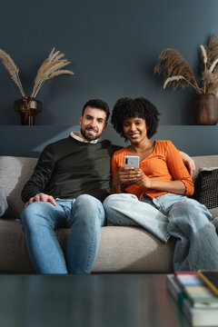 Portrait of happy young multiracial couple relaxing on sofa, feeling safe at home
