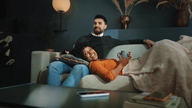 Young married couple resting in the couch together at home, enjoying television show 
