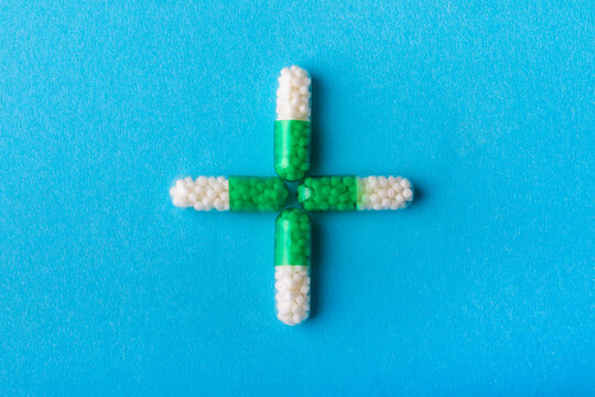 Four green and white capsules arranged in a plus sign on a vibrant blue background, symbolizing healthcare and medicine.