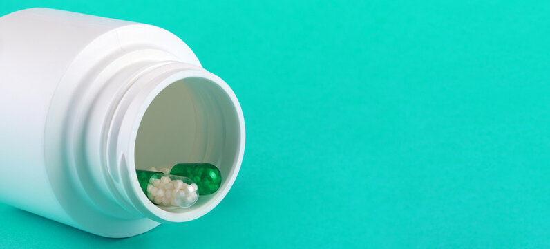White pill bottle tipped over with green and white capsules on turquoise background, ideal for healthcare and pharmaceutical concepts.