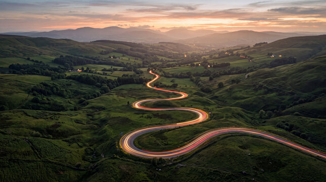 Winding country road cuts through green hills at sunset aerial view