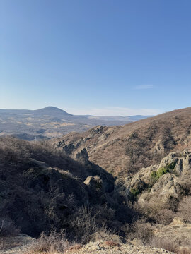 Rocky mountain hills with dry vegetation under clear blue sky.