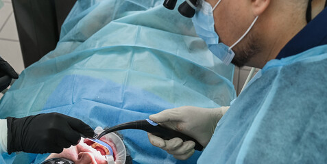 Dentist and  assistant treating male patient, using dental drill and saliva suction while patient undergoes oral treatment in modern dental clinic © illustrissima