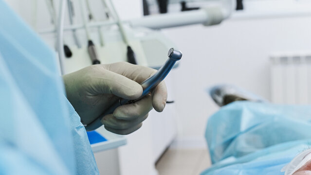 A dentist inserts a burr into a contra-angle handpiece to prepare a bone bed for an implant or to work with an implant system during a dental implant placement procedure. Close-up, face removed.