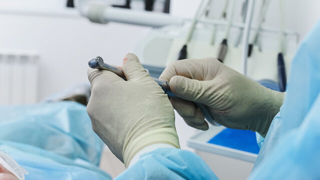 A dentist inserts a burr into a contra-angle handpiece to prepare a bone bed for an implant or to work with an implant system during a dental implant placement procedure. Close-up, face removed.