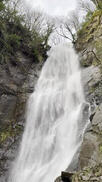 Vertical video of a powerful high waterfall in the mountains.