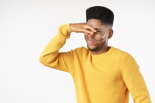 Young African man reacting to bad smell isolated over white background, disgusted male covering nose, expressing unpleasant odor, discomfort, aversion, hygiene problem and negative reaction concept