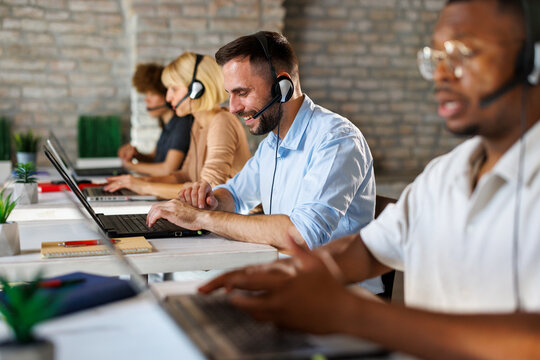 Smiling customer service team working in a modern call center office with headsets and laptops