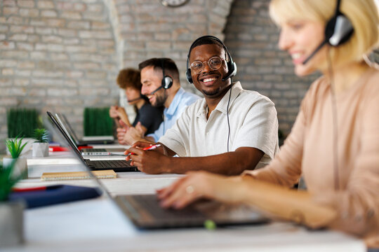 Smiling customer service team working in a modern call center office with headsets and laptops