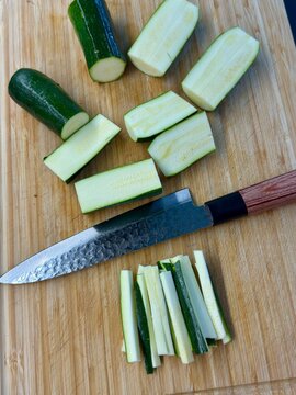 Fresh green zucchini cut into thin julienne sticks on a wooden cutting board with a Japanese chef knife. This image highlights culinary prep food slicing and cooking step by step.