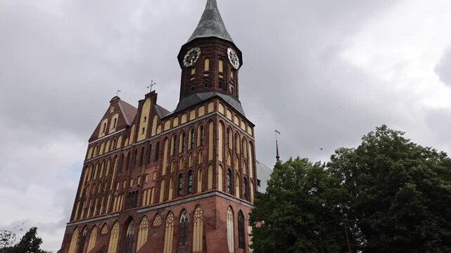 View of the historic red-brick Gothic architecture of Kaliningrad Cathedral with surrounding trees and a cobblestone square in Kaliningrad, Kaliningrad Oblast, Russia.
