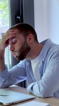 Frustrated young man finishing his work on a laptop at home, feeling stressed and tired from a difficult project, showing emotions of burnout and exhaustion from overworking