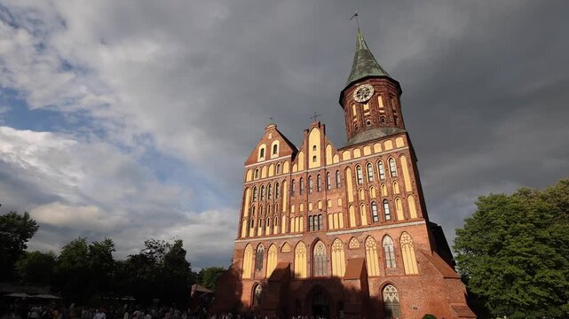 View of the historic brick Gothic Kaliningrad Cathedral with its tall clock tower set against a dramatic cloudy sky in Kaliningrad, Kaliningrad Oblast, Russia.