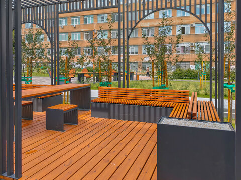Modern wooden gazebo with seating benches in urban public park. Landscaped area with sapling trees and pavement. modern urban park seating, public plaza design