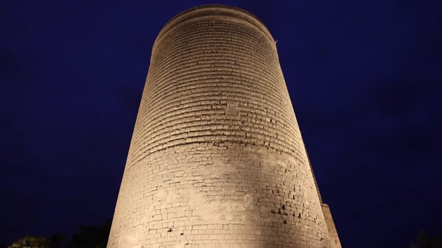 View of the historic Maiden Tower illuminated at night with people walking nearby in the old town of Baku, Baku, Azerbaijan.