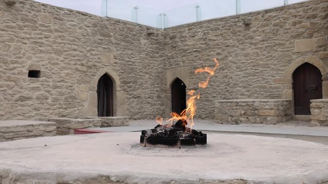View of eternal flame burning at the Ateshgah Fire Temple surrounded by stone walls and arched doorways in Baku, Baku, Azerbaijan.