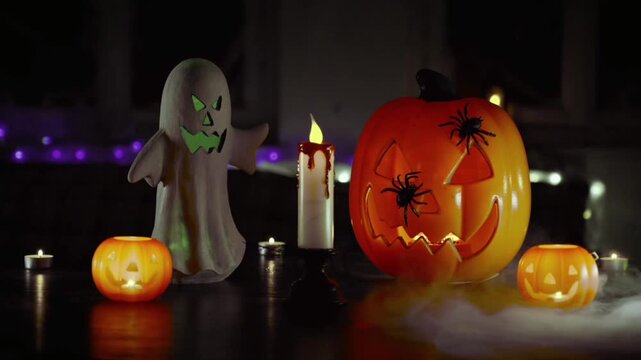 In the center, there is a bright orange carved pumpkin (jack-o'-lantern) with a black spider resting on it, a white ghost figure with a menacing face, and a melting, lit candle.
