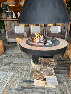 A cozy interior features a modern fireplace with a large chimney, surrounded by wooden stools and comfortable seating. 