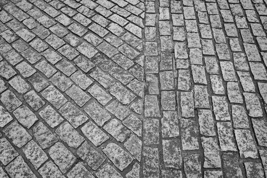 High-angle black and white shot of a classic cobblestone pavement featuring two distinct paving patterns meeting together.