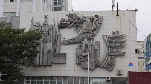 View of a detailed Soviet-era metal relief sculpture on a building facade in Vladivostok, Primorsky Krai, Russia.