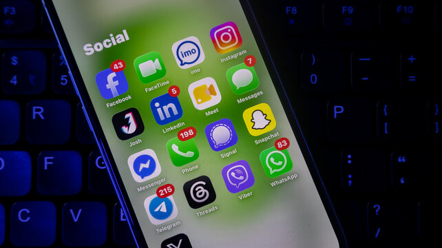 Social media application icons on smartphone screen over dark keyboard background.