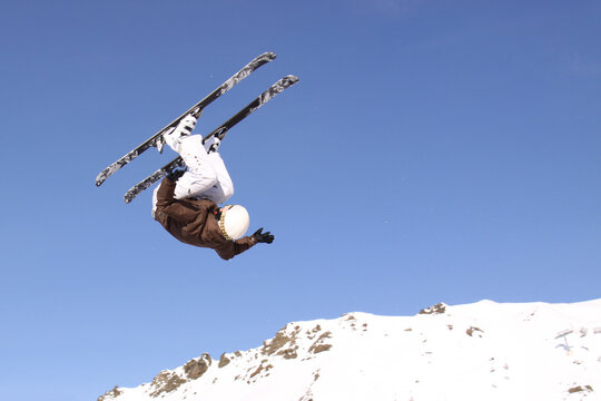 Freestyle skier performing backflip trick in mid air against blue sky
