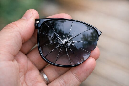 A person holding a broken pair of sunglasses, likely due to an accident or careless handling