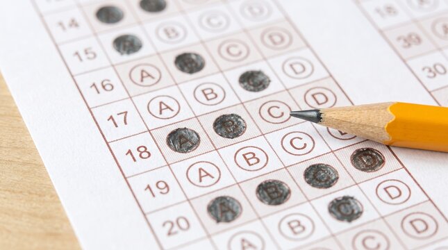 Yellow pencil filling answer bubbles on multiple choice test sheet. Standardized exam answer sheet close up.